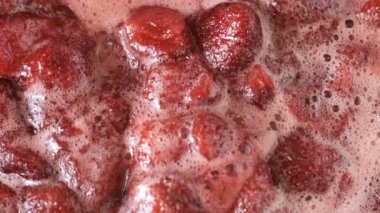 Çilek reçelini kendi suyunda yapma süreci. Gaz sobası makro video çekiminde açık bir kaseye şeker eklenmesi.