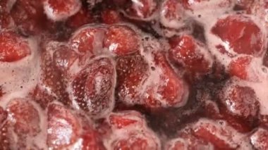 Çilek reçelini kendi suyunda yapma süreci. Gaz sobası makro video çekiminde açık bir kaseye şeker eklenmesi.