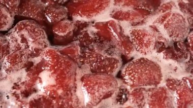 Çilek reçelini kendi suyunda yapma süreci. Gaz sobası makro video çekiminde açık bir kaseye şeker eklenmesi.