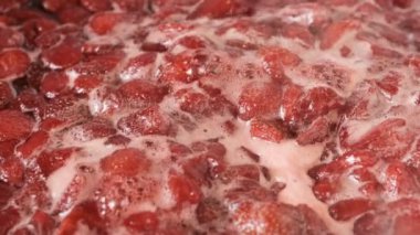 Çilek reçelini kendi suyunda yapma süreci. Gaz sobası makro video çekiminde açık bir kaseye şeker eklenmesi.