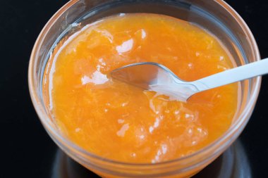 Siyah bir ayna yüzeyinde duran cam bir rosette tatlı bir kayısı reçeli, makro fotoğraf.