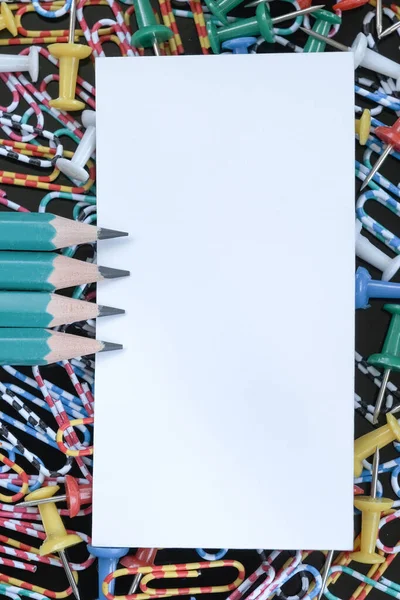 White rectangular sheet of note paper with pencils close-up on a black background macro photography