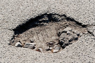 Büyük bir çukur, parlak güneş ışığı altındaki bir mahalle caddesinde toprak ve kayaları ortaya çıkarır..