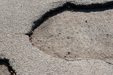 Büyük bir çukur, parlak güneş ışığı altında pürüzsüz asfalt yüzeyini bozar..