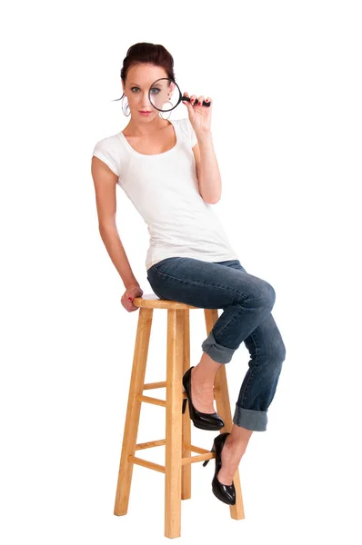 Pretty girl seated on a stool holding a magnifying glass — Stock Photo, Image