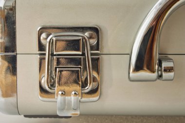 Modern, bej bir ekipman çantasının parlak krom mandalına yakın çekim. Temiz, endüstriyel tasarım güvenlik, koruma ve profesyonel araçları sembolize eder. Şirket ve teknoloji temaları için mükemmel.