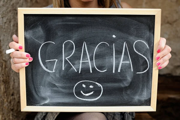 blackboard held with both hands of woman with the word thank you in spanish written by hand with white chalk