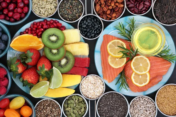 Health food for a healthy heart with fresh vegetables, fruit, nuts, seeds, pulses, grains, cereals, herbs and olive oil. Super food concept high in omega 3 fatty acid, antioxidants, anthocyanins, minerals and vitamins.