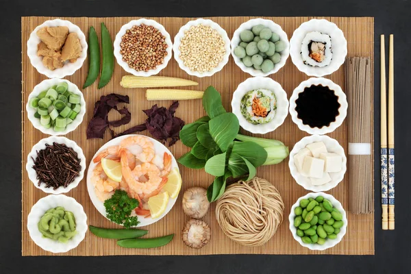 Macrobiotic Japanese food concept with seafood, sushi, miso and wasabi  paste and nuts, tofu, kuchika tea, vegetables, soba noodles, soy, tofu, with foods high in protein, antioxidants, vitamins and minerals.  On bamboo and slae background, top view.
