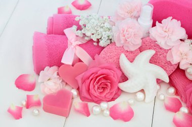 Güzellik Bakımı temizlik ürünleri ile pembe gül ve karanfil çiçek, kalp ve kabuk şeklinde sabun, vücut losyonu, süngerler, ex foliating bodur ve yıkama bezler ile dekoratif kabukları ve inci beyaz ahşap zemin üzerinde.