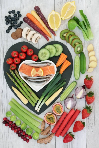 Super food concept for good health with fresh fish, fruit and vegetables on heart shaped slate  . High in omega 3 fatty acids, antioxidants, anthocyanins, minerals, vitamins and dietary fibre. Top view.