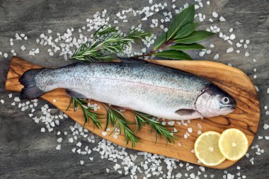 Gökkuşağı alabalığı sağlıklı kalp gıda biberiye ve defne yaprağı otlar, ders deniz tuzu ve mermer zemin üzerine limon ile zeytin bir ahşap panosuna. Omega 3 yağ asidi yüksek.
