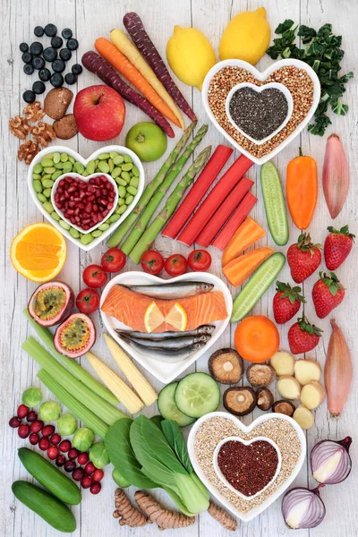 Health food for a healthy life with fresh fish, nuts, seeds, grains, fruit and vegetables on heart shaped  dishes and loose on rustic background. High in omega 3 fatty acids, antioxidants, anthocyanins, minerals, vitamins and dietary fiber. Top view.