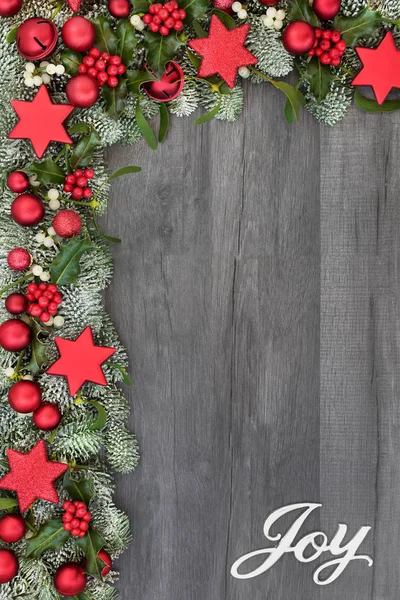 Christmas background border with silver joy sign, red ball, bell  and star bauble decorations, holly, spruce fir and mistletoe on rustic grey wood. Christmas festive theme.