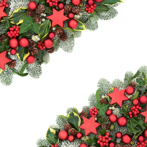 Christmas background border with red bauble decorations, winter flora of holly berries, snow covered spruce pine, ivy, pine cones and mistletoe on white background with copy space.