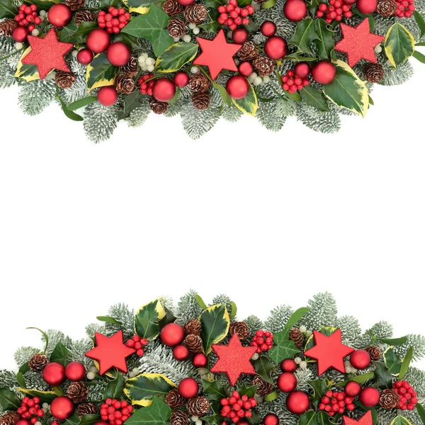 Christmas Festive background border with red bauble decorations, winter flora of holly berries, snow covered spruce pine, ivy, pine cones and mistletoe on white background with copy space.