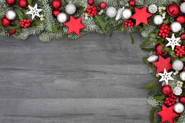 Christmas festive background border with star, bell, ball and pine cone bauble decorations with holly, spruce fir and mistletoe on rustic grey wood background.