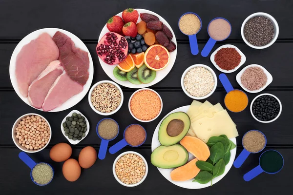 Health food for body builders high in protein including meat, dairy, dietary supplement powders, chlorella tablets, grains, cereals, fruit, vegetables and seeds on dark wood background.