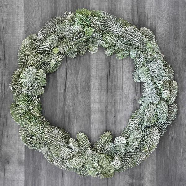 Winter and Christmas snow covered spruce fir wreath on rustic grey wood  background.