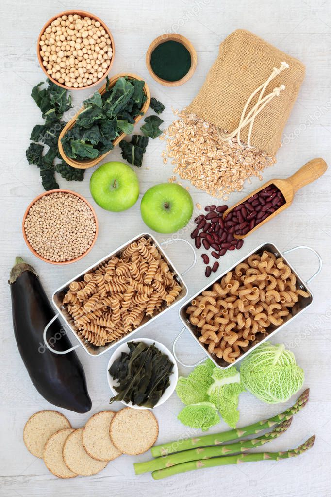 High fibre health food concept with fresh vegetables and fruit, whole wheat pasta, pulses, cereals, grains, oatmeal crackers and spirulina powder. High in antioxidants, vitamins and minerals.