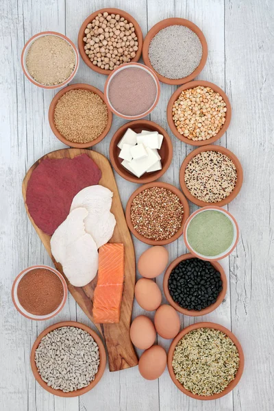 High protein food selection with meat, fish, vegan tofu, legumes, dairy, supplement powders, grains and seeds. Hgh in dietary fibre, antioxidants and vitamins. Top view on rustic wood background.