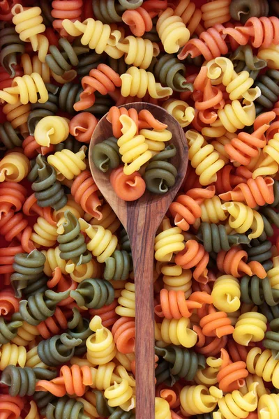 在橄榄木勺子上的 Trotolle 三色意大利面和松散的形成一个抽象的背景 — 图库照片