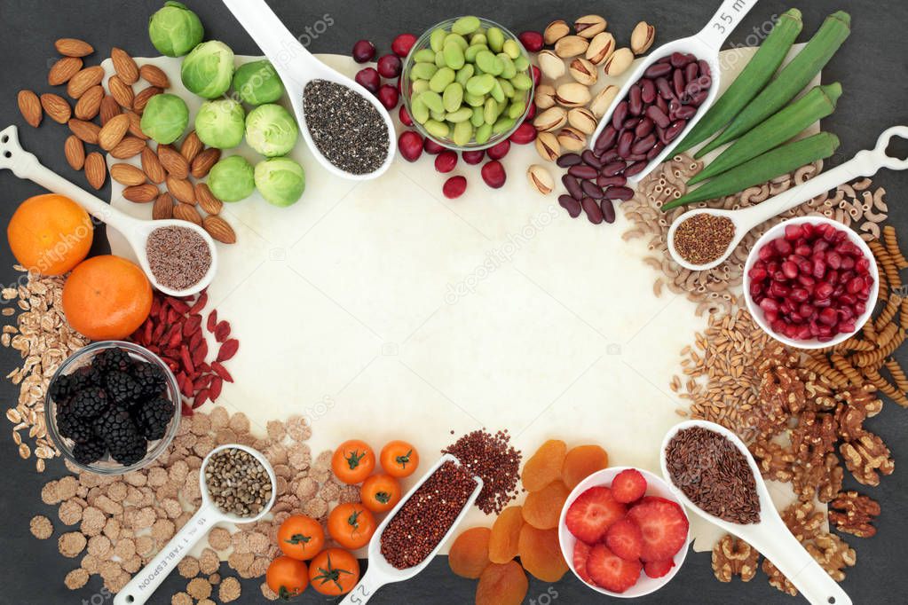 High fibre super food background border with fruit, vegetables, seeds, nuts, whole wheat pasta, cereals & grains. Foods with omega 3, anthocyanins, antioxidants & vitamins. On parchment paper & slate.