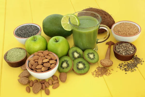 Healthy fruit juice smoothie drink for fitness with matcha powder, almonds, flax, hemp and chia seed, with fresh fruit on yellow wood background. High in omega 3, antioxidants, vitamins and dietary fibre.