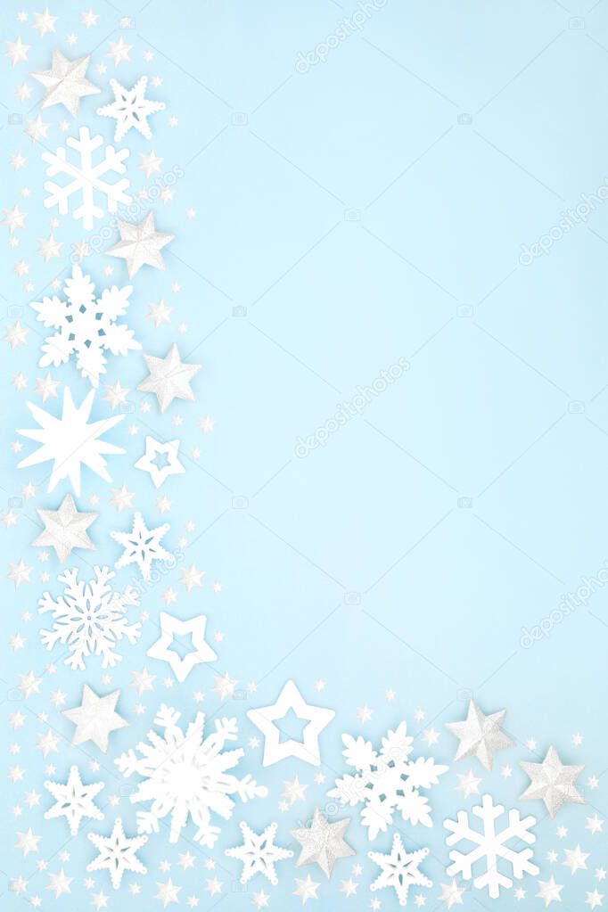 Christmas snow covered border with white star, snowflake & ball bauble decorations on pastel blue background. Xmas & winter & New Year composition for the festive holiday season. 