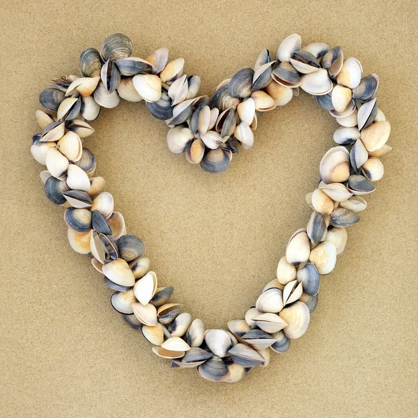 砂の背景にハート型の貝の花輪 ロマンチックなシンボルと夏休みのコンセプト — ストック写真