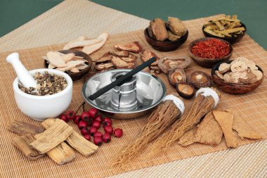Çin bitkisel ilaç seçimi ve moxibustion terapisinde bambu hasırı üzerinde havan ve tokmak ve yeşil arka planda kullanılan moxa çubuğu..