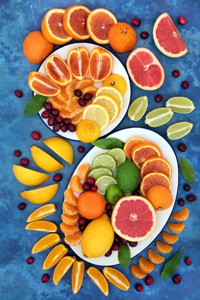 Summer sunshine citrus fruit with oranges, lemons, limes, grapefruit & cranberries high in antioxidants, anthocyanins, lycopene, fibre & vitamin c. Immune boosting health care concept. On mottled blue.