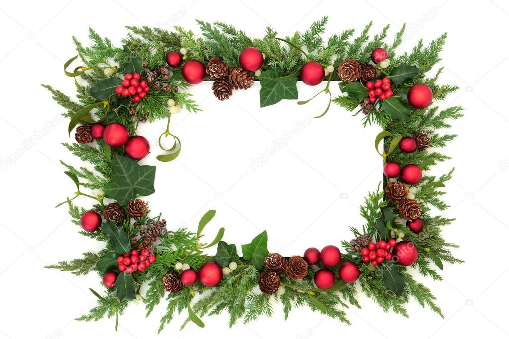 Festive Christmas border on white background with red bauble decorations & winter greenery of holly, ivy, mistletoe, juniper fir & cedar cypress. Decorative element for the holiday season. Copy space.