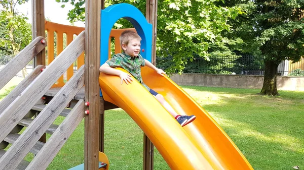 young boy plays with a slide in the park