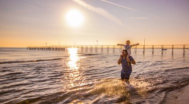 Baba ile oğlu onun omuzlarında denizde su içeri girer
