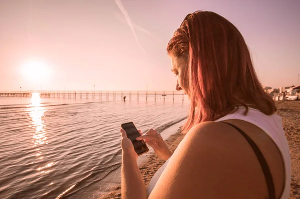 Frau Beobachtet Handy Auf Dem Meer Während Des Sonnenuntergangs — Stockfoto