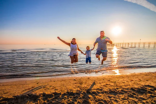 快乐的家庭在日落的阳光下在岸边跳跃 — 图库照片