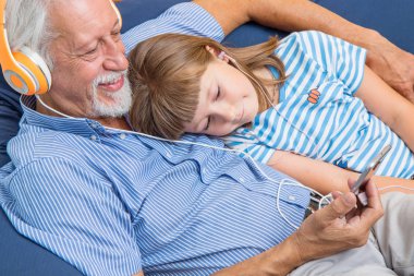 grandfather and grandson with headphones listen to music hugging each other on the couch  clipart