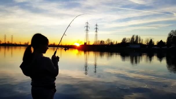 日落时在池塘里钓鱼的年轻女孩 — 图库视频影像