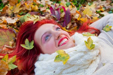 Güzel bir kadın kırmızı sonbahar yaprağının üzerinde yatıyor.