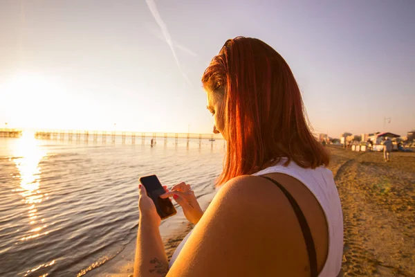 Όμορφη Γυναίκα Γράφουν Στο Smartphone Στην Παραλία Στο Ηλιοβασίλεμα — Φωτογραφία Αρχείου