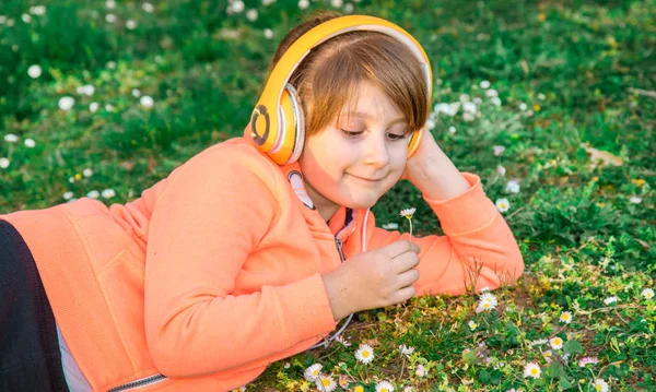 Dziewczyna, leżąc na trawie słucha muzyki i podnosi stokrotki — Zdjęcie stockowe