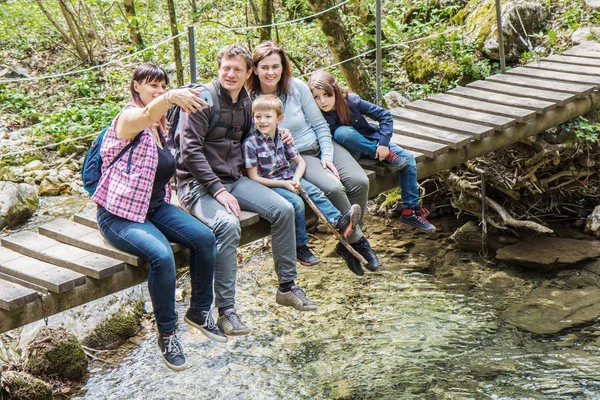 Família feliz estão sentados em uma ponte de madeira no meio de para — Fotografia de Stock