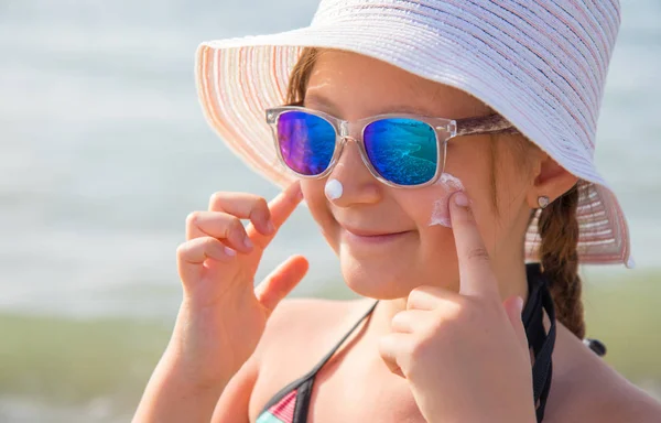 Smiling girl with hat smears protective face cream on the beach — Stock Photo, Image