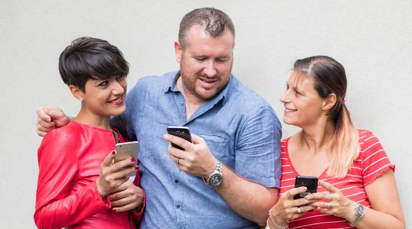Skupina přátel, kteří se usmívají a hledají smartphone — Stock fotografie