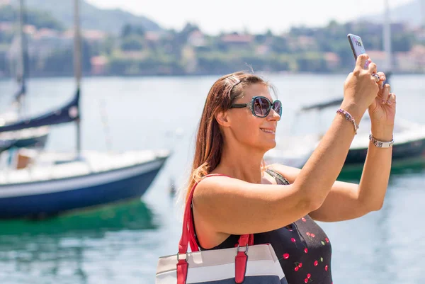 Sorrindo mulher está tomando uma selfie perto do lago — Fotografia de Stock