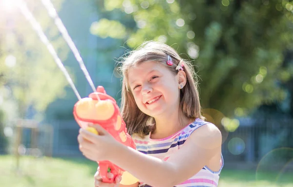 Klein meisje spelen met waterpistool in het Park op een zonnige dag — Stockfoto