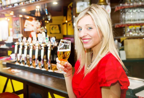 Young woman holding glass of beer in a pub — Stock Photo, Image