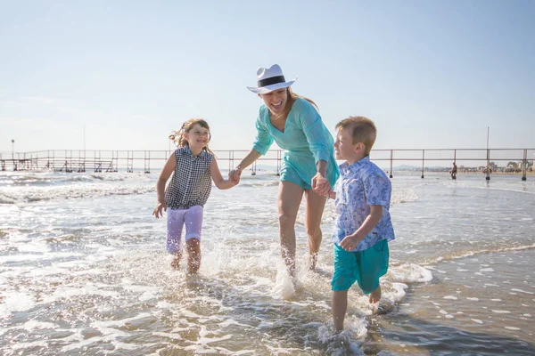 Moeder en kinderen spelen in de zee op het strand — Stockfoto