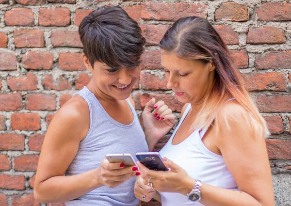 İki mutlu arkadaş akıllı bir telefonu paylaşıp izliyorlar. — Stok fotoğraf